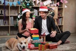 Überraschen Sie zwei Mitarbeiter und einen Hund in der Nähe, indem Sie Geschenke geben, während Sie vor dem Firmenurlaub am Büroarbeitsplatz sprechen, ist für die Weihnachtsfeier und die Neujahrsfeier dekoriert. foto