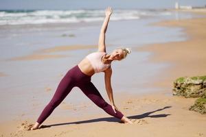 Kaukasische blonde Frau, die Yoga am Strand praktiziert