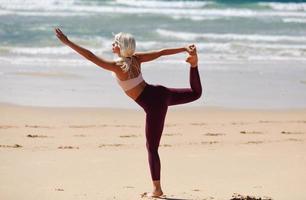 Kaukasische blonde Frau, die Yoga am Strand praktiziert