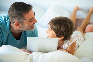 Vater mittleren Alters mit ihrer achtjährigen Tochter mit digitalem Tablet im Schlafzimmer. foto