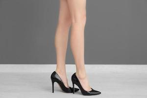 Beine der jungen Frau in Schuhen mit hohen Absätzen, die in der Nähe der grauen Wand stehen