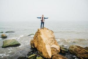 Reisender Mann steht auf einem Felsen gegen ein schönes Meer foto