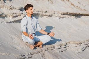 Mann sitzt in Meditationshaltung am Sandstrand