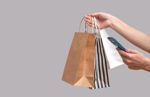 Frau online von einem Mobiltelefon aus einkaufen. weibliche Hände mit Paketen auf grauem Hintergrund isoliert, Textfreiraum foto
