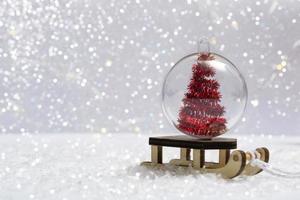 auf dem Schnee - ein Schlitten mit einer Weihnachtskugel in einem Weihnachtsbaum auf einem Hintergrund von Bokeh-Lichtern Nahaufnahme. vertikales Foto