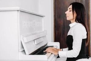 schöne Frau im weißen Kleid, die auf weißem Klavier spielt foto