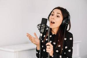 Schöne Frau mit Kopfhörern singt ein Lied in der Nähe eines Mikrofons in einem Tonstudio. Platz für Text oder Werbung foto