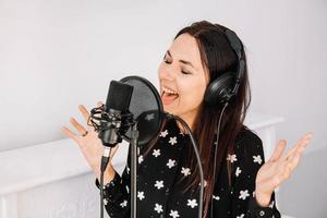 Schöne Frau mit Kopfhörern singt ein Lied in der Nähe eines Mikrofons in einem Tonstudio. Platz für Text oder Werbung foto