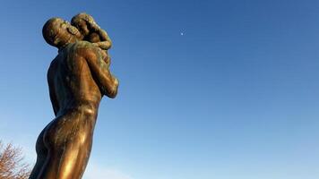 Östersund, Schweden, März 11, 2022. das Bronze- Statue von ein Mann halten ein Kind gegenüber das Nachmittag Mond. foto