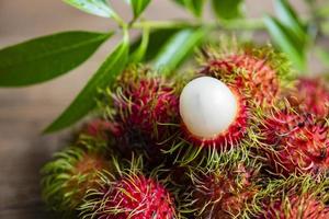 frisches und reifes Rambutan süße tropische Früchte geschältes Rambutan mit Blättern, Rambutanfrucht auf Holzuntergrund Ernte aus dem Garten