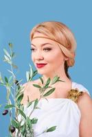 griechische blonde fröhliche frau in nationaltracht mit gefälschtem olivenzweig in ihren händen foto
