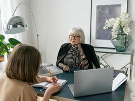 Ältere stilvolle Frau mit junger Frau, die Arbeitsaufgaben im Büro bespricht. Geschäft, Kommunikation, Arbeit, Alter, Zusammenarbeit, Mentoring-Konzept foto