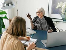 Ältere stilvolle Frau mit junger Frau, die Arbeitsaufgaben im Büro bespricht. Geschäft, Kommunikation, Arbeit, Alter, Zusammenarbeit, Mentoring-Konzept foto