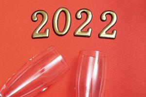 Draufsicht flach neues Jahr Mockup auf rotem Hintergrund mit Zahlen, Champagner und Gläsern. Nahaufnahme. neues Jahr 2022, mit Textfreiraum foto