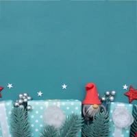 Weihnachtsflacher Hintergrund mit Gnom, Geschenken, Beeren und Kiefer auf türkisfarbenem Hintergrund