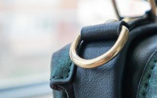 Ovaler Ring aus Metall mit Goldschlaufe, der an einer Ledertasche befestigt ist. selektiver Fokus. Teil für eine sichere Verbindung zwischen zwei Objekten. Nähzubehör in Ringform zum Nähen von Taschen, glänzend. foto