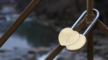 ein Schloss aus ineinander verschlungenen Herzen, eingesperrt auf einem Geländer als Zeichen ewiger Liebe. zwei Herzen in Form eines gelben Liebesschlosses hängen am Geländer der Brücke foto