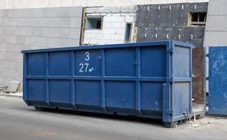 Metall haltbarer blauer industrieller Mülleimer für Müll im Freien auf der Baustelle. großer Abfallkorb für Haus- oder Gewerbemüll. ein Haufen Müll.