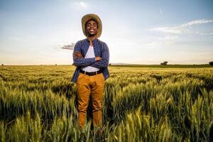 Porträt von afrikanisch Farmer im seine wachsend Weizen Feld. er ist zufrieden mit Fortschritt von Pflanzen. foto