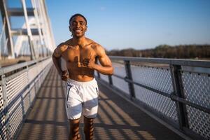 jung Afroamerikaner Mann ist Joggen auf das Brücke im das Stadt. foto