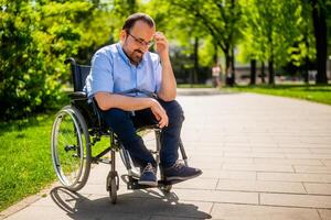 Porträt von glücklich Mann im Rollstuhl. er ist genießen sonnig Tag im Stadt Park. foto