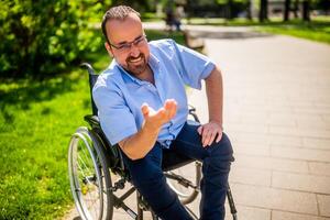 Porträt von glücklich Mann im Rollstuhl. er ist genießen sonnig Tag im Stadt Park. foto