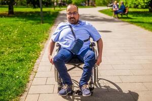 Porträt von glücklich Mann im Rollstuhl. er ist genießen sonnig Tag im Stadt Park. foto