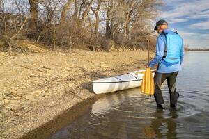 Senior männlich Paddler mit Expedition geschmückt Kanu auf ein See Ufer im früh Frühling, boedecker Reservoir im Nord Colorado foto