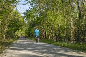 männlich Radfahrer ist Reiten ein falten Fahrrad auf katy Weg in der Nähe von Rocheport, Missouri, Frühling Landschaft. das katy Weg ist 237 Meile Fahrrad Weg umgewandelt von ein alt Eisenbahn. foto