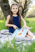 ein Kind Mädchen ist lesen ein Buch im das Park foto