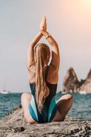 Yoga auf das Strand. ein glücklich Frau meditieren im ein Yoga Pose auf das Strand, umgeben durch das Ozean und Felsen Berge, fördern ein gesund Lebensstil draußen im Natur, und inspirierend Fitness Konzept. foto