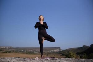 ein Frau ist tun Yoga auf ein Felsen im ein schön Landschaft foto