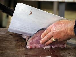 Detail von Hand von ein Fischhändler Hacken Schwertgisch beim frisch Fisch Meeresfrüchte beim ortigia Syrakus Sizilien Fisch Markt Italien foto