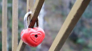 schäbiges rotes Schloss in Herzform. Valentinstag Liebe Konzept. Ein an einem Metallgeländer hängendes Vorhängeschloss ist ein Zeichen der ewigen Liebe. die Tradition, eine Burg mit einem Zaun zu verbinden foto