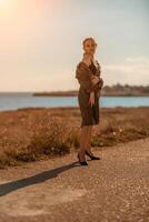 Porträt blond Meer Kap. ein Ruhe jung blond im ein aufgeknöpft khaki Regenjacke Spaziergänge entlang das Strand, unter ein Regenjacke ein schwarz Rock und oben foto