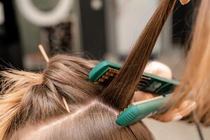 das Friseur bereitet vor ein Frau, macht ein Frisur mit Locken mit ein Eisstockschießen Eisen. lange Licht braun natürlich Haar. selbst Pflege Konzept. foto