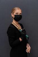 ein Frau im ein schwarz Kleid halten ein Haar Lockenwickler. sie ist tragen ein Maske. Konzept von Vorsicht und Verantwortung im das Gesicht von ein Pandemie. foto