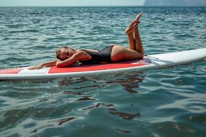 Frau Saft Meer. Sport Mädchen auf ein Surfbrett im das Meer auf ein sonnig Sommer- Tag. im ein schwarz Baden Anzug, er Lügen auf ein Saft im das Meer. sich ausruhen auf das Meer. foto