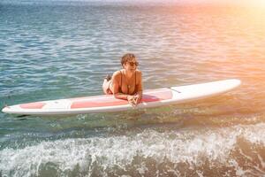 Frau sup Meer Reise. Sport Mädchen auf ein Surfbrett im das Meer auf ein sonnig Sommer- Tag. im ein schwarz Baden Anzug, er sitzt auf ein Sapa im das Meer. sich ausruhen auf das Meer. foto