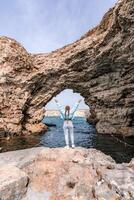 Meer Frau Felsen Grotte. ein Frau im ein Blau Jacke steht auf ein Felsen über ein Cliff über das Meer und sieht aus beim das tobt Ozean. Mädchen Reisender ruht, denkt, Träume, genießt Natur. foto
