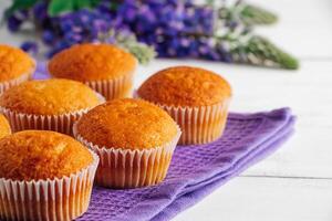 köstlich Muffins und lila Lupine Blumen auf Weiß hölzern Hintergrund. foto