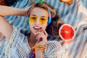 aufgeregt Mädchen auf Strand Handtuch. Boho Zubehör. tropisch Früchte. Gelb sonnenbrille.top Sicht. foto