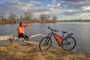 Senior männlich Radfahrer mit ein Mountin Fahrrad auf ein Ufer von See im Colorado, Winter oder früh Frühling Landschaft foto