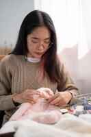 ein schön asiatisch Frau ist Fokussierung auf Handnähen ein Muster auf Stoff auf ein Stickerei rahmen. foto