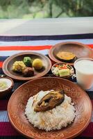 kuder Bhat, Hilsa khichuri Combo mit Salat, Aubergine, borhani und Chui Pitha serviert im Gericht isoliert auf Matte oben Aussicht von indisch und Bangladesch Essen foto