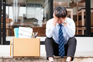 betrübt Mann sitzt draußen Büro mit seine Besitz nach dem Rücktritt. foto