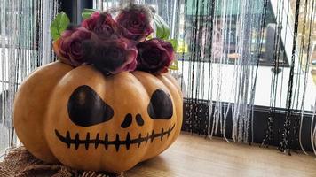 Kürbis mit einem gruseligen Gesicht auf einem Holztisch. Das Innere des Hauses ist mit Kürbissen und Spinnweben für den Halloween-Feiertag dekoriert.