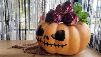 Kürbis mit einem gruseligen Gesicht auf einem Holztisch. Das Innere des Hauses ist mit Kürbissen und Spinnweben für den Halloween-Feiertag dekoriert.