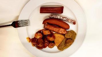 Verschiedene deutsche Würstchen auf einem weißen Teller mit einer Gabel in einer Kneipe. traditionelles deutsches essen in einem teller. Carrivurst, Bratwurst, Thüringer, Weißwurst, Nürnberg, Bockwurst, Nekvurst foto