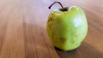 grüner fauler Apfel auf einem hölzernen Hintergrund. grüner Apfel auf einem alten hölzernen Hintergrund, Ansicht von oben. Bio saftiger Bio-Apfel hässlich, mit essbaren Mängeln liegt auf einem Holztisch. kein hässliches essen foto